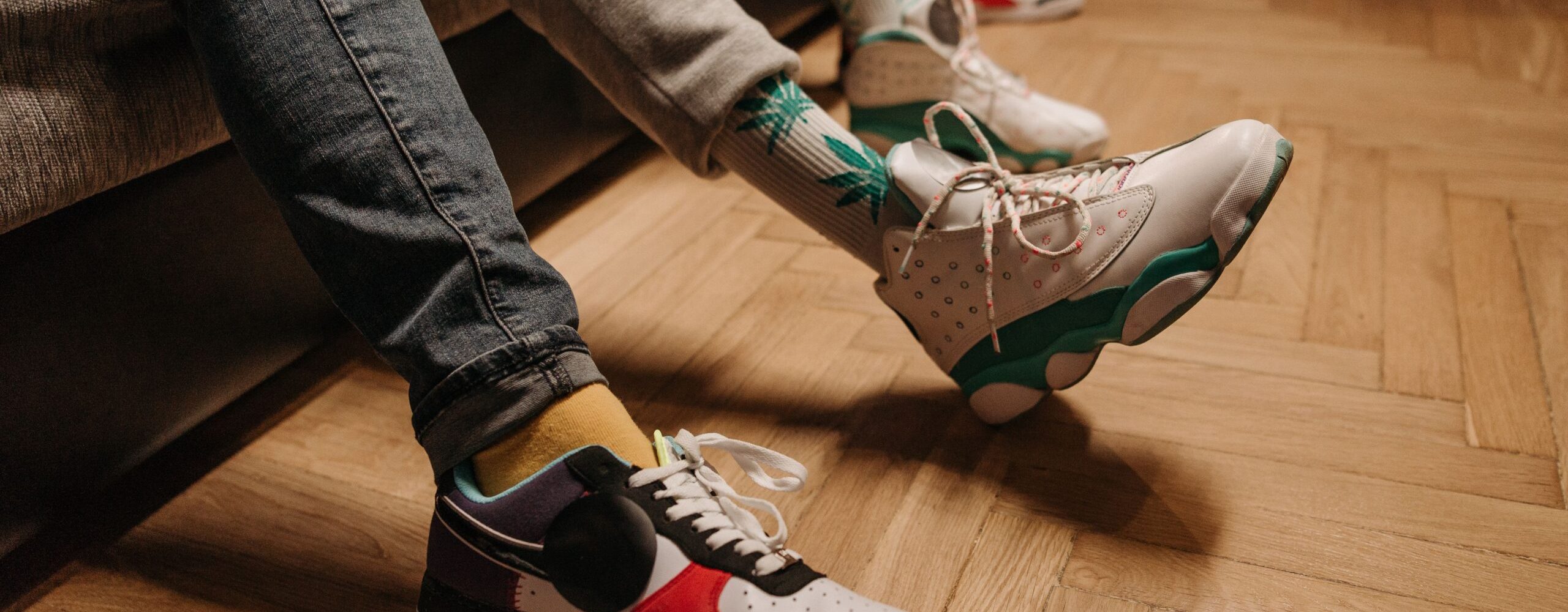 Close-up of legs in colorful sneakers relaxing indoors on wooden floor.